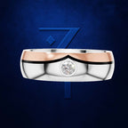 A two-tone wedding band featuring a polished silver body, a rose gold chevron accent across the top, and a single round-cut clear gemstone in the center. The ring is presented on a textured dark blue background with a stylized blue '7' logo behind it.