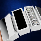 White jewelry boxes arranged on a dark blue background, with one open box showing four clear gemstones in a silver setting.