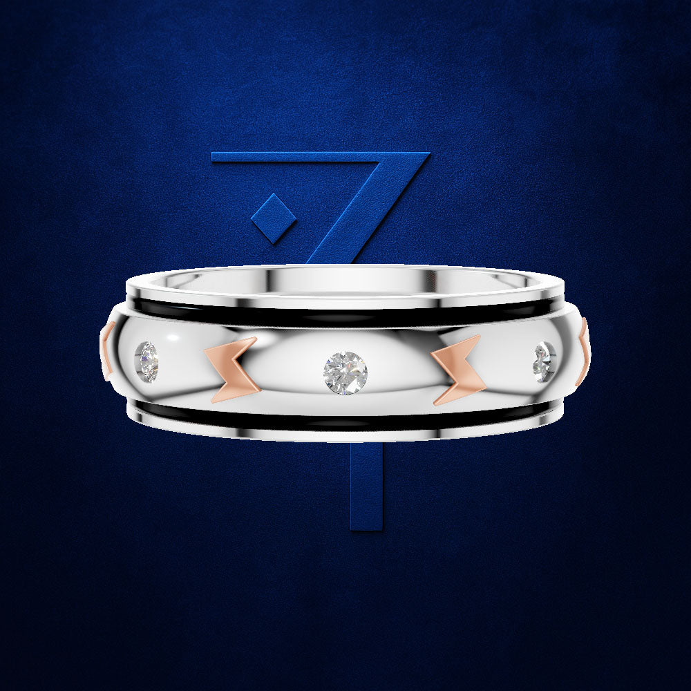 A silver-toned band ring with a polished center, black inlay bands, three clear gemstones, and three rose-gold chevron accents, shown against a dark blue textured background with a blue stylized '7' logo behind it.