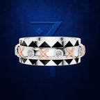 A double-band ring set in silver and rose gold, featuring a top band with a black and white geometric triangle pattern and a bottom band with alternating rose gold X-shaped links and round clear gemstones, set against a dark blue textured background with a blue stylized '7' logo.