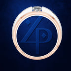 A close-up studio shot of a circular ring with a rose-gold-toned outer band, a white inner band, and a clear gemstone at the top. The center is a deep blue insert featuring embossed initials 'ZP'.