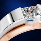 Close-up of a ring with a rectangular clear gemstone in a two-tone setting, featuring a silver band and a rose gold band, set against a dark blue textured background.