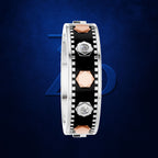 A silver-toned band ring with a black inlay, rose gold geometric accents, and small clear gemstones, shown on a dark blue textured background.