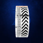 A wide silver band ring featuring a central channel with a row of clear pavé diamonds and a bold black and white chevron pattern, accented by a rose gold top bar, set against a textured dark blue background.