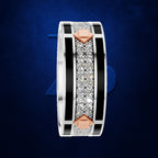 A wide silver-toned ring with black enamel bands, a central row of clear stones, and two rose-gold diamond-shaped accents on either side, shown on a dark blue textured background.