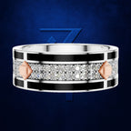 A wide silver-toned ring with a central channel of clear pavé stones, bordered by black inlay and accented with rose gold geometric shapes, shown on a dark blue textured background.