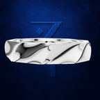 A polished silver ring with a sculpted, wavy, fluid-like pattern, shown floating against a textured dark blue background with a matching blue stylized '7' logo behind it.