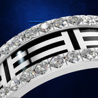 A close-up of a silver-toned ring set with multiple clear round and marquise-cut gemstones, featuring a bold black-and-white geometric pattern on the band, against a deep blue background.