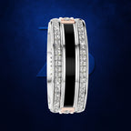 A wide silver-toned band ring featuring a central black inlay, bordered by rows of clear pavé-set stones on both sides, with small rose gold end accents, displayed on a dark blue textured background.