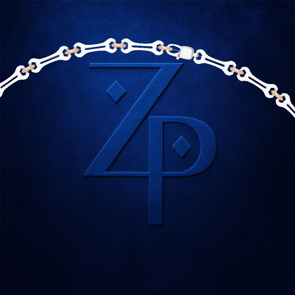 A close-up of a dark blue textured surface featuring a large embossed stylized 'ZP' monogram, with a white chain draped over the top edge and small warm metallic links visible between the chain segments.