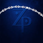 A close-up of a dark blue textured surface featuring a large embossed stylized 'ZP' monogram, with a white chain draped over the top edge and small warm metallic links visible between the chain segments.