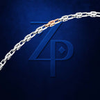 A close-up of a silver chain necklace with a rose gold accent link, displayed against a textured dark blue background with a stylized 'ZP' logo.