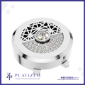 A round silver-toned jewelry box lid with a geometric cutout pattern on top, a central clear gemstone, and a semi-circular section of clear pavé stones. The brand name PLATIZEM is visible at the bottom.