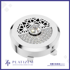 A round silver-toned jewelry box lid with a geometric cutout pattern on top, a central clear gemstone, and a semi-circular section of clear pavé stones. The brand name PLATIZEM is visible at the bottom.