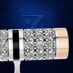 A close-up of a luxury cylindrical watch or accessory featuring a silver-toned bezel, a central cluster of clear pavé-set round diamonds, a black vertical stripe, and a rose gold-toned end cap, set against a textured dark blue background with a stylized blue '7' logo.