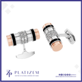 A pair of cylindrical cufflinks by Platinzem, featuring a silver-toned body with black enamel stripes, a central diamond-encrusted band, and rose gold end caps, shown on a white background with the Platinzem brand logo at the bottom.