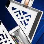 A close-up of a geometric white pendant or brooch with a blue cutout pattern, shown against a textured royal blue background. The piece has polished silver-toned edges and a rose gold-toned loop at the top.