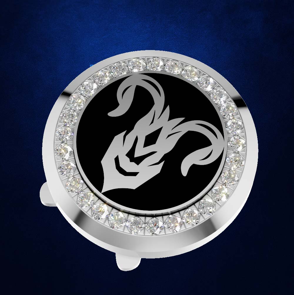 A circular silver-toned accessory with a black center featuring a white zodiac symbol, surrounded by a border of clear rhinestones, shown on a dark blue textured background.