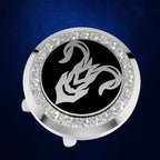 A circular silver-toned accessory with a black center featuring a white zodiac symbol, surrounded by a border of clear rhinestones, shown on a dark blue textured background.