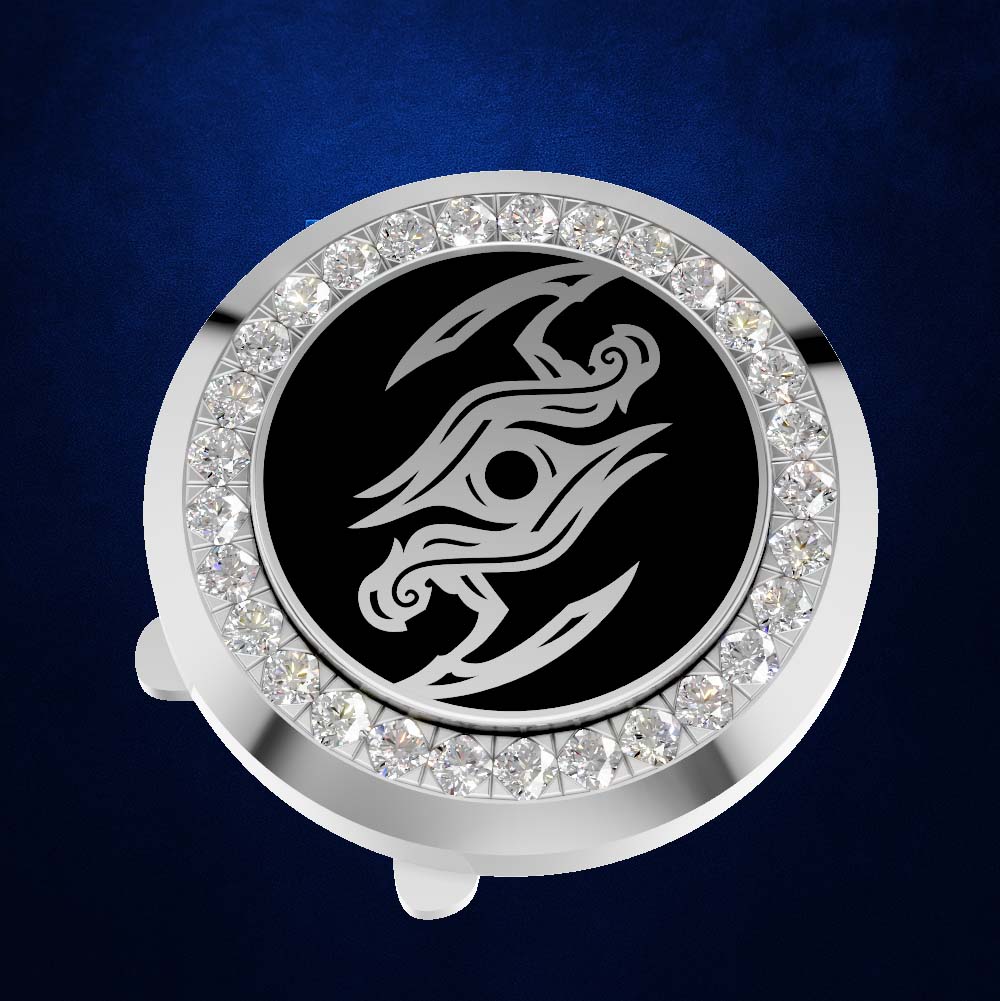 A round silver-toned golf ball marker with a black center featuring a stylized silver graphic, surrounded by a halo of clear rhinestones, shown on a dark blue textured background.
