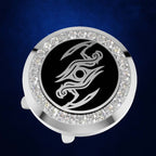 A round silver-toned golf ball marker with a black center featuring a stylized silver graphic, surrounded by a halo of clear rhinestones, shown on a dark blue textured background.