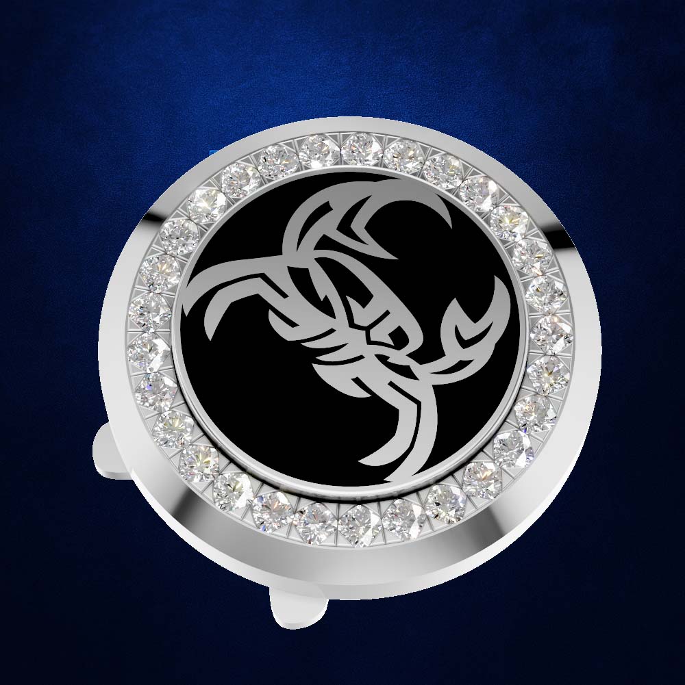 A circular silver-toned accessory with a black center featuring a stylized silver scorpion graphic, surrounded by a border of clear rhinestones, shown on a dark blue textured background.