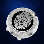 A round silver-toned accessory with a black center featuring a stylized lion face, surrounded by a halo of clear rhinestones, shown on a dark blue textured background.