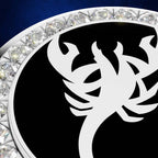 A close-up of a circular black and white emblem or medallion with a stylized white scorpion-like silhouette on a black field, surrounded by a border of clear faceted stones on a dark blue background.