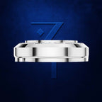 A polished silver-toned metal watch crown or watch component centered on a textured dark blue background, with a stylized blue number 7 behind it.