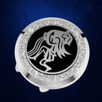 A round silver-toned ring holder or watch stand featuring a black center with a stylized lion emblem, surrounded by a border of clear rhinestones, set against a dark blue textured background.