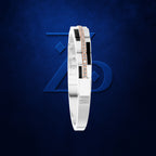 A white and black geometric bangle bracelet with a central rose gold diamond-studded stripe, displayed against a textured dark blue background with a subtle geometric logo.