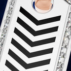 A close-up of a white rectangular accessory with bold black chevron stripes and a circular clear crystal detail, bordered by sparkling rhinestone-like embellishments on a dark blue background.