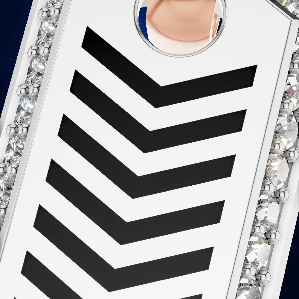 A close-up of a white rectangular accessory with bold black chevron stripes and a circular clear crystal detail, bordered by sparkling rhinestone-like embellishments on a dark blue background.