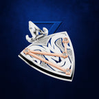 A luxury fashion accessory, likely a pendant or brooch, featuring a shield-like design with silver and white scrollwork, blue inlay, rose gold bars, and clear rhinestones, set against a textured dark blue background.