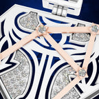 A close-up of a white jewelry box with intricate navy blue cutout patterns, sparkling clear rhinestones, and pale pink ribbon ties with round crystal centers.