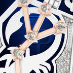 Close-up of a luxury watch dial featuring a white and navy blue shield-like motif with rose gold bars and clear gemstones.