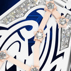 Close-up of a luxury watch dial featuring white and navy blue geometric Arabic numerals, rose gold hour markers with clear round gemstones, and diamond-studded silver bezel sections.