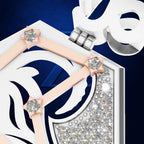 A close-up studio shot of a white and navy geometric pendant or charm with pale pink ribbon-like accents, clear gemstones, and a silver clasp on a dark blue background.