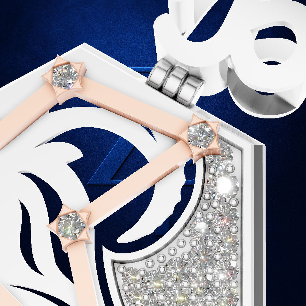 A close-up studio shot of a white and navy geometric pendant or charm with pale pink ribbon-like accents, clear gemstones, and a silver clasp on a dark blue background.