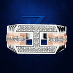 A wide structured ring with a white and rose gold band, heavily set with clear diamonds. The center features a bold geometric design with cutouts showing a blue background, set against a dark blue textured backdrop with a subtle blue '7' logo behind it.