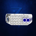 A white ring with a grid of clear gemstones, a blue inset side panel, and a blue geometric side accent, shown against a dark blue background with a matching blue stylized emblem.