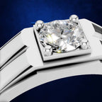 Close-up of a silver-toned ring with a large round brilliant-cut diamond set in a square bezel, shown against a dark blue background.