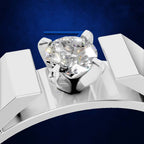 A close-up studio shot of a solitaire engagement ring with a round brilliant-cut diamond set in a polished silver-colored band, presented on a dark textured blue background.