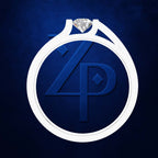 A white ring-shaped pendant or emblem with a clear faceted gemstone at the top and a large embossed blue monogram inside, centered on a dark blue textured background.