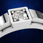 A close-up of a silver-toned ring with a square bezel holding a large clear round gemstone, set against a deep blue background.