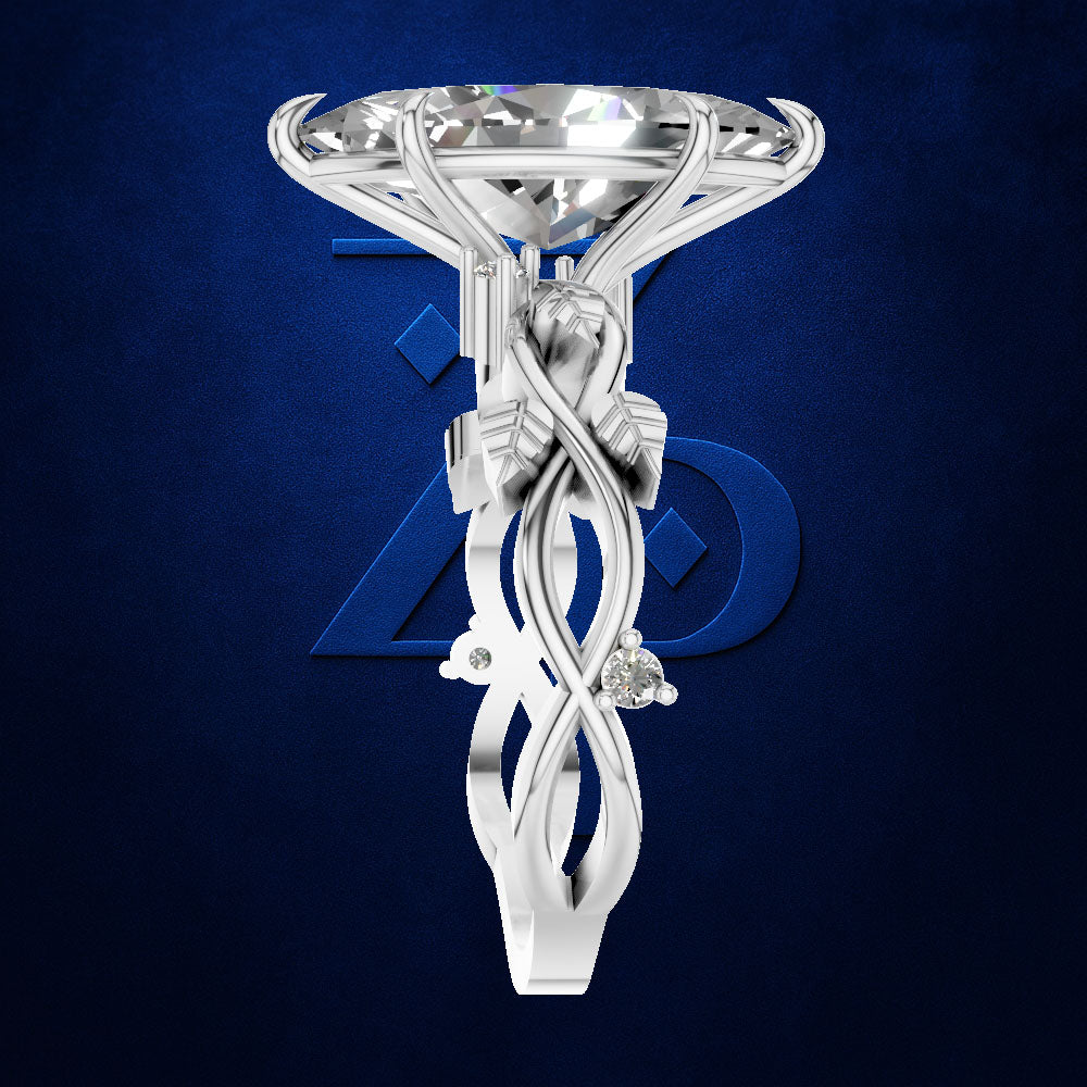A white gold or platinum engagement ring featuring a large round brilliant-cut diamond and an intricate sculpted shank with swirling details and a small accent stone, set against a dark blue textured background with a subtle blue logo.