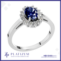 A silver-plated halo ring featuring a round deep blue sapphire center stone and surrounded by small clear accent stones, shown on a white background with the Platisem brand logo at the bottom.