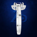 A silver-toned halo ring featuring a round deep blue gemstone and baguette side stones, shown from the top-down view against a textured dark blue background.