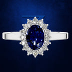 A silver ring featuring a large oval deep blue sapphire center stone surrounded by a halo of round clear diamonds, set against a dark blue textured background.