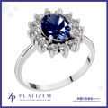 A platinum ring featuring a large oval-cut deep blue sapphire center stone, surrounded by a halo of round brilliant-cut clear diamonds, set on a polished silver-colored band. The brand logo 'PLATIZEM' is visible at the bottom of the image.